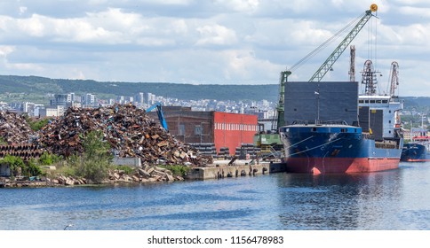 A Large Heap Of Scrap Metal In The Processing And Loading Area In Sea Cargo Ships. A Scrap Heap On An Industrial Quay In The Cargo Port Area Is Prepared For Loading And Transportation By Sea