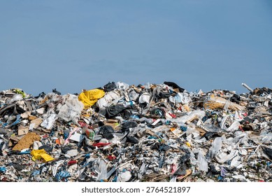 Large heap of unsorted trash and plastic waste at a landfill under a clear blue sky. Concept of environmental pollution, consumerism, and the global waste crisis. Industrial landfill site showing various discarded materials like bags, plastic, and cardboard. Ecological disaster and waste management challenge in a modern society.