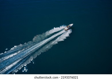 Large High Speed Boat Fast Moving Diagonal Air View. White Boat With People Moving Fast On Dark Blue Water. Top View. White Orange Boat In Motion.