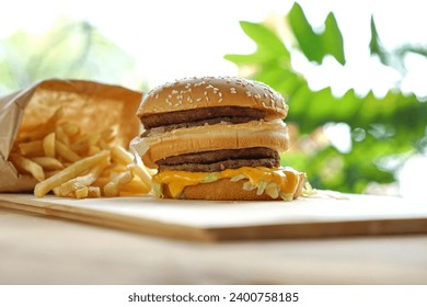 Large homemade burgers on wooden platter Ingredients: sauce, sesame, lettuce, tomato, onion, cucumber, cheese, bacon and seasoned minced meat. There are french fries in a paper bag on the side and a b - Powered by Shutterstock