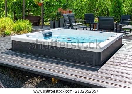 Large hot tub embedded in the backyard terrace. A sunny summer's day in the shelter of a green garden. Everyday luxury and relaxation in your own backyard. Spa complex, vacation and traveling concept.