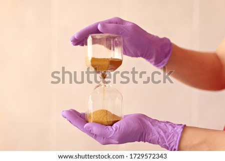 Large hourglass with medical gloves. Hands hold hourglass.