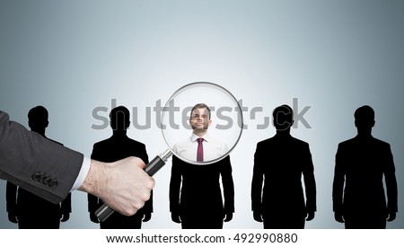 Large human hand with magnifying glass examining man silhouettes against light gray wall. Concept of recruitment. Mockup