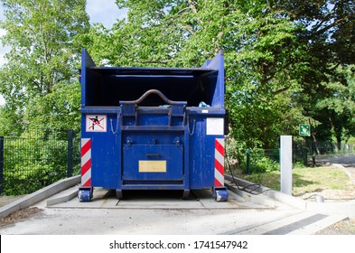large hydraulic garbage compactor surrounded by trees on a sunny afternoon