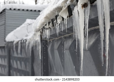 large icicles hanging from the roof. ice melting icicles and snow melting in spring. gray concrete fence under the snow
