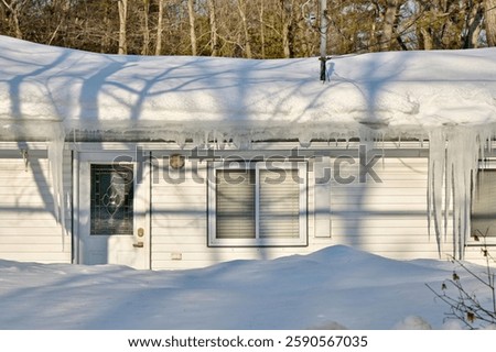 Large icicles and ice dams form at the edge of the snow-covered roof above frozen eavestrough gutter