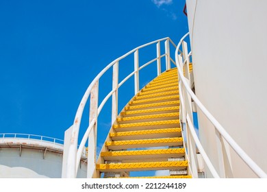 Large Industrial tanks for oil with a walkway up and down of oil storage tank metal stairs on the side blue sky.