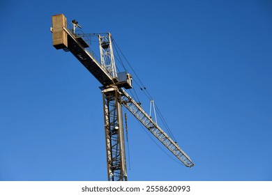 A large industrial tower crane designed for heavy lifting, standing tall against a clear blue sky at a construction site. - Powered by Shutterstock