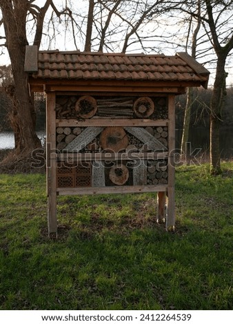 large insect hotel for bees, spiders and butterflies with a roof made of red roof tiles and a filling of bricks, branches, wood and other natural objects on a green lawn