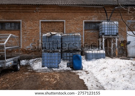 Large intermediate bulk containers IBC tanks standing in the snow outside an old brick industrial warehouse