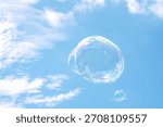 Large, iridescent soap bubbles floating against a bright blue sky scattered with soft white clouds.