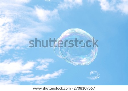 Large, iridescent soap bubbles floating against a bright blue sky scattered with soft white clouds.