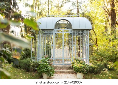 Large iron blue gazebo for relax outdoor. Wedding decorations. exterior Romantic alcove. Decor autumn terrace. Wrought metal gazebo in summer garden. Flowers in pots near porch. Sofa in spring gazebo.