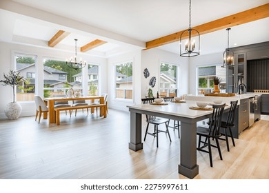 large kitchen with beamed ceiling hardwood floors white countertop grey cabinets and set dining table with large windows bar cart view to living room - Shutterstock ID 2275997611