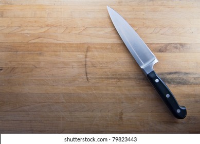 A Large Knife Sits On A Worn Butcher Block Counter Top