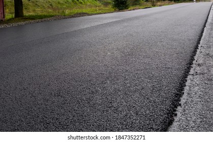 A large layer of fresh hot asphalt. Layer of asphalt raw material in a shallow depth of field. Rollers rollin fresh hot asphalt on the new road. Road construction. Construction of a new road.