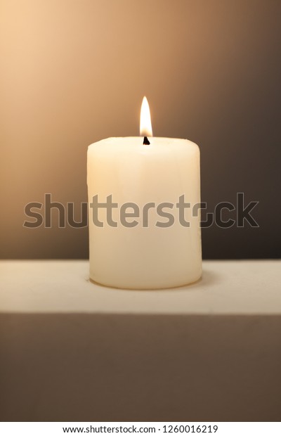 Large lighted\
burning white candle on a shade background. Monochrom single\
vertical holidays\
composition.