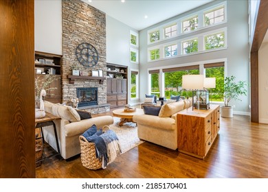 Large living room with exposed beam ceiling stone fireplace expansive windows hardwood flooring and built in shelving