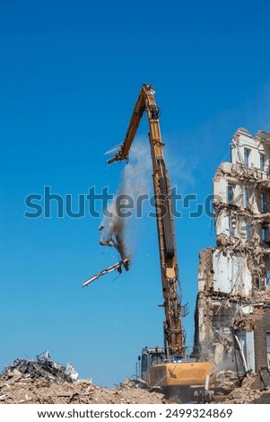 Large long armed demolition machine seen demolishing a building, dropping debris.