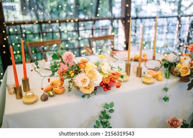 A Large, Long, Decorated, Wooden Table And Chairs, Covered With A White Tablecloth With Dishes, Flowers, Candles, Stands Outdoor Near The Forest In Nature. Wedding Banquet. Lights On Background
