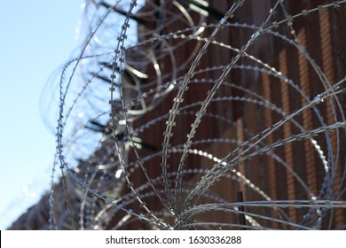 large loops of sharp razor wire hang on bollard style border wall at the US-Mexico border 5058