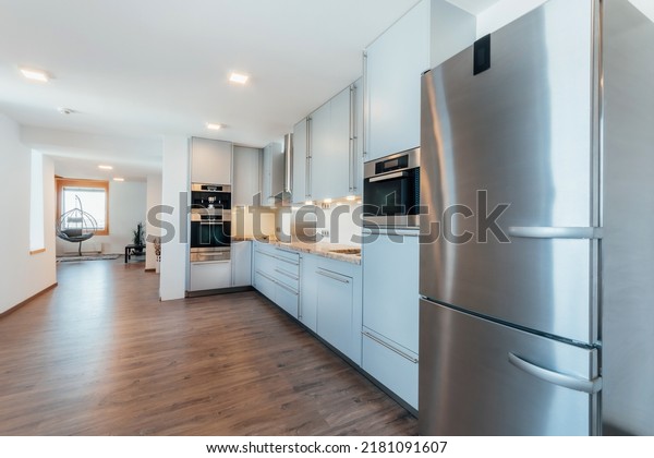 Large\
luxury kitchen unit made of light blue laminate, glass and marble.\
It is equipped with premium built-in appliances. The kitchen is lit\
by warm spot LED lights. The floor is\
wooden.