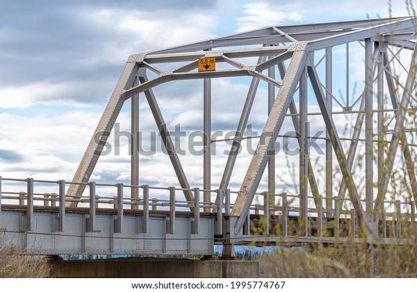 Large man made structure steel bridge\
spanning across Nisutlin Bay in township of Teslin flowing to the\
Yukon River in norther Canada during spring summer time with cloudy\
mountains background.