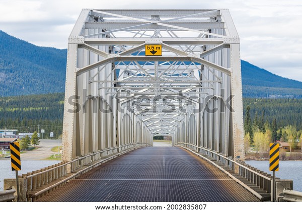 Large man made structure steel bridge\
spanning across Nisutlin Bay in township of Teslin flowing to the\
Yukon River in northern Canada during spring summer time with\
cloudy mountains\
background.