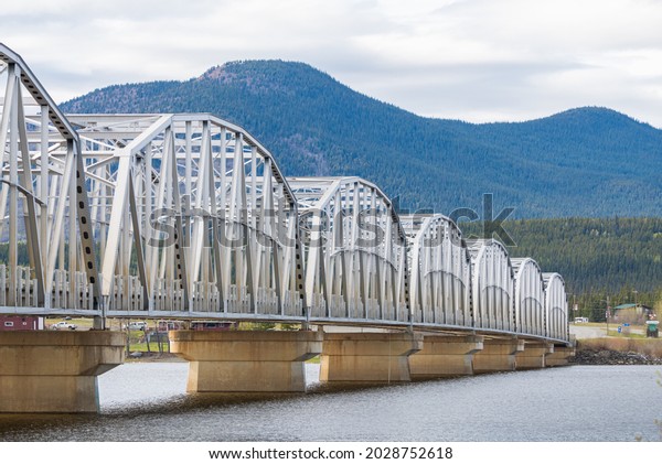 Large man made structure steel bridge\
spanning across Nisutlin Bay in township of Teslin flowing to the\
Yukon River in northern Canada during spring summer time with\
cloudy mountains\
background.	\
