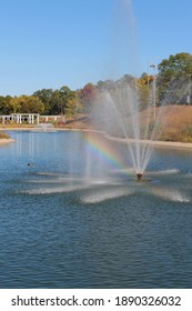 A large, manmade pond with a water fountain and a rainbow in the water spray in the midst of Sinnissippi Gardens in Rockford, Illinois, USA