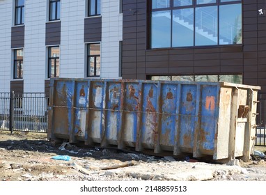 A large metal blue dumpster near the wall of the house