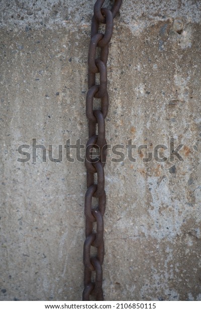 large metal chain hanging against grungy concrete\
exterior industrial wall weathered with pock marks large links on\
chain dividing the image in two vertically vertical format room or\
space for type 