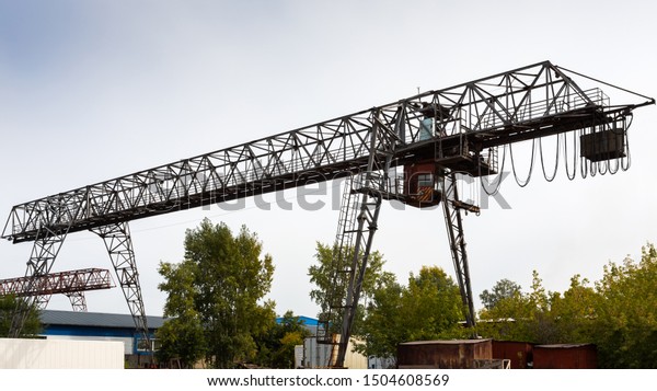 large\
metal gantry crane at a construction site, in the background\
industrial warehouses for storing goods. Type of bearing metal\
structures of gantry crane against the blue\
sky