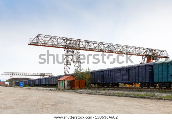 Large metal gantry\
cranes at a on the railway platform, standing on freight wagons for\
storing goods. Type of bearing metal structures of gantry crane\
against the blue sky