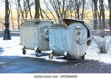 Large metal garbage cans, recycling bins, trash containers on wheels outside in the winter snowy park at daytime. 