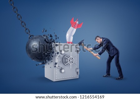 A large metal safe box stands unbroken and whole under the hits of a wrecking ball, a rocket and a man with a hammer. Safe bank. Personal account. Reliable banking system.