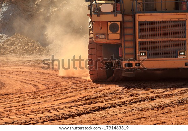 Large\
mining dump truck lifts orange dust on\
wheels