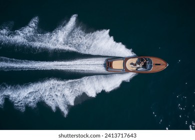 A large modern high-speed wooden luxury boat moves on blue water, top view. Expensive wooden boat, man and woman in motion on the water making a white trail looking like air. - Powered by Shutterstock