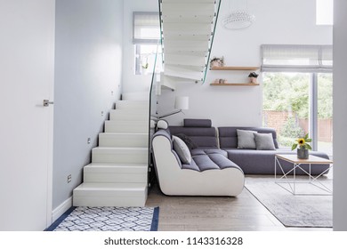 Large, Modern Sofa In A White Living Room Interior With Natural Light And Stylish Staircase With Glass Barricade