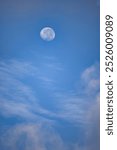 A large moon is in the sky above a blue sky. The sky is mostly clear with a few clouds scattered throughout. The moon is the main focus of the image, and it is shining brightly against the blue sky