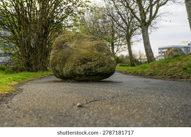 Large mossy boulder blocking quiet paved park pathway