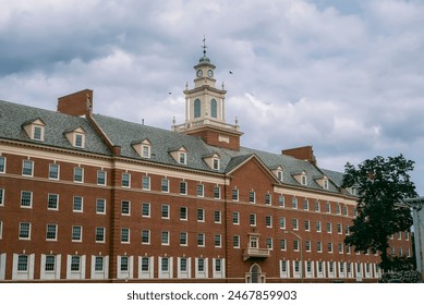 A large, multi-story academic building with a clock tower under a cloudy sky.