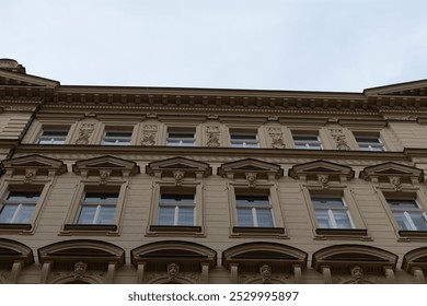 A large, multistory building featuring numerous windows stands prominently against a backdrop of a gray, overcast, cloudy sky above