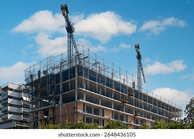 A large, multi-story building under active construction, featuring scaffolding, cranes, and exposed framework against a clear sky.