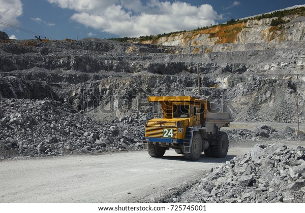 Large multi-toned mining truck in a limestone\
quarry on the background of blue sky with clouds. Quarry equipment.\
Mining industry.