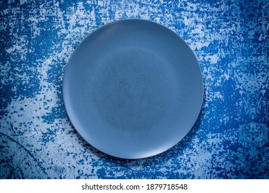 Large Navy Blue Plate On Blue Rustic Background. Used Plate With Scratches. Selective Focus. Shot From Above