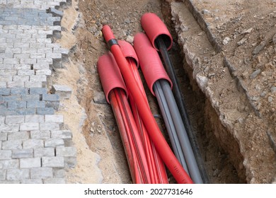 A large number of electric and high-speed Internet Network cables in red corrugated pipe are buried underground on the street covered with cobblestones.  - Shutterstock ID 2027731646