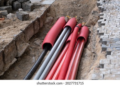 A large number of electric and high-speed Internet Network cables in red corrugated pipe are buried underground on the street covered with cobblestones.  - Shutterstock ID 2027731715