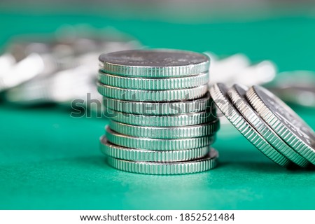 a large number of silver-colored metal coins stacked together on a green background, legal tender that is used for payments in the state, beautiful coins close-up the same coin value foreign currency