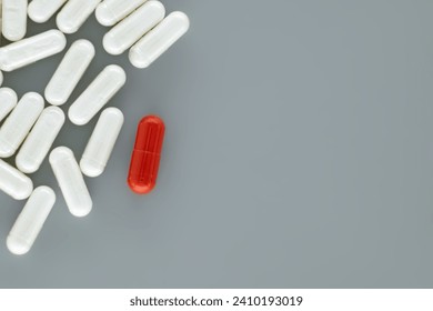 Large number of white pills scattered on a gray surface, among the white pills a single red pill drawing focus, symbolically representing uniqueness or distinction